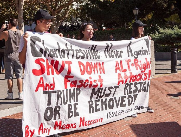 Protesters with By Any Means Necessary hold a banner reading 