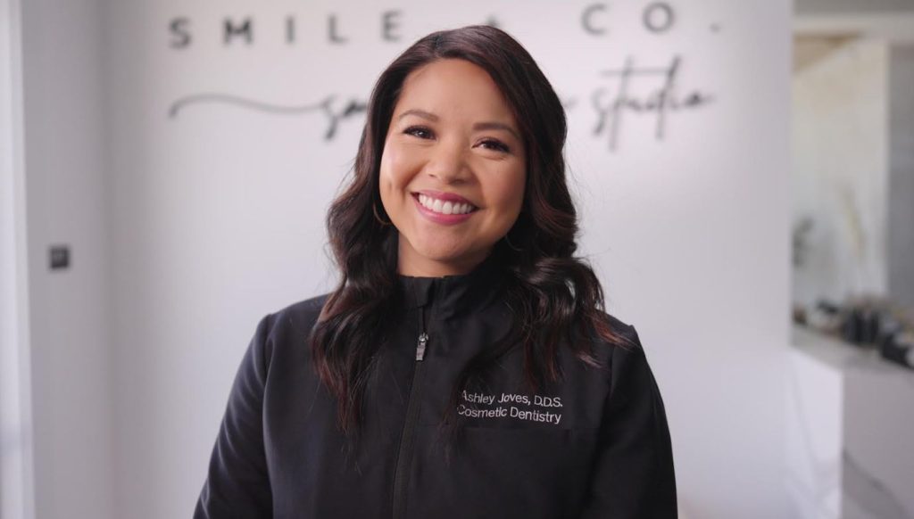 Ashley Joves wearing a sweater with the logo from her cosmetic dentist practice