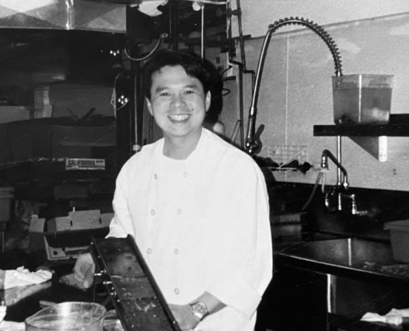 An early photo of Charles Pham in the kitchen wearing a traditional white chef's uniform