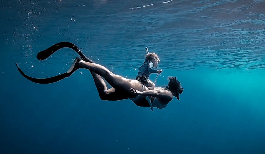 Young child is underwater scuba diving on the back of an adult